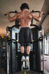 Muscular guy doing pull ups on exercise machine