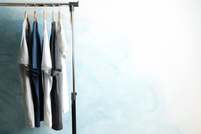 Rack with blank t-shirts on blue background, space for text