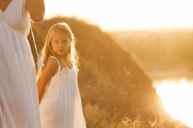 Female child in summer dress standing with unrecognizable woman outside at dusk
