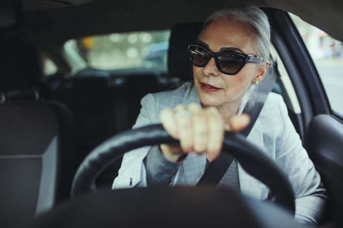 Stylish mature businesswoman driving her car and looking away