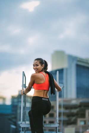 Rear view of a woman in fitness clothes standing on rooftop stairs and turning back