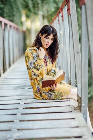 Female sitting on a rural bridge enjoying reading