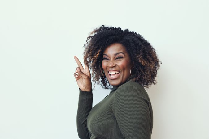 Joyful Black woman laughing while making the peace sign