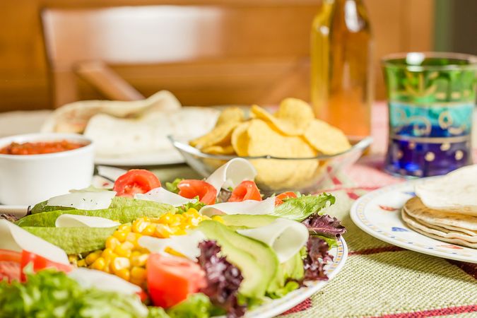Traditional mexican food with a plate of fresh salad, tortillas, chicken fajitas, nachos and a bowl of spicy sauce
