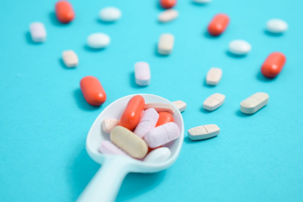 Scattered pills on plastic spoon on blue table