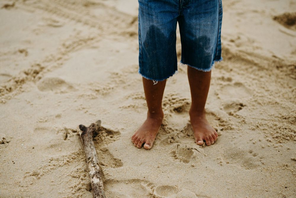 Crop child standing on sand near stick