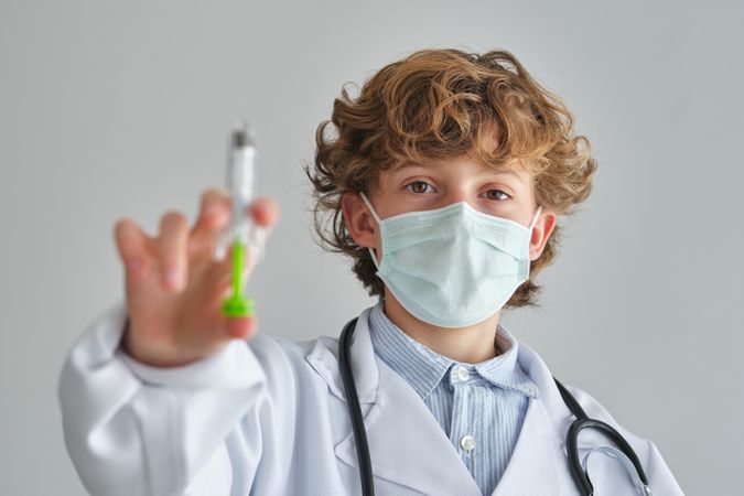Boy in medical mask with toy syringe