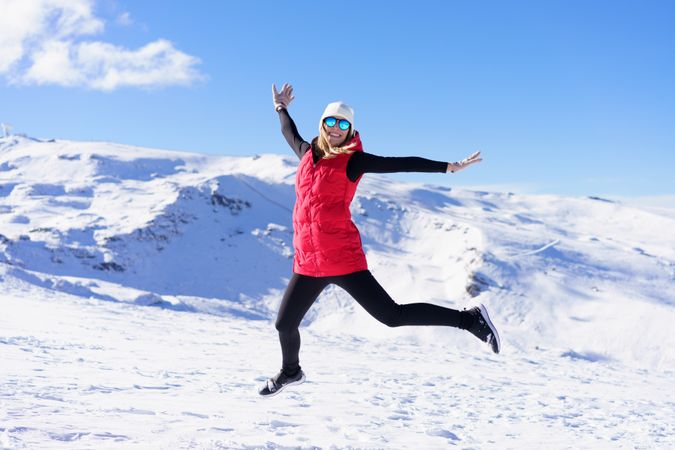 Woman in winter gear jumping and smiling on snowy mountain