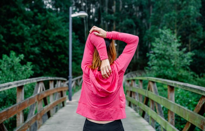 Unrecognizable sportswoman doing stretching arms outdoors