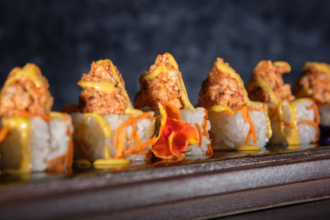 Appetizing sushi topped with salmon and fresh sauce served on wooden tray