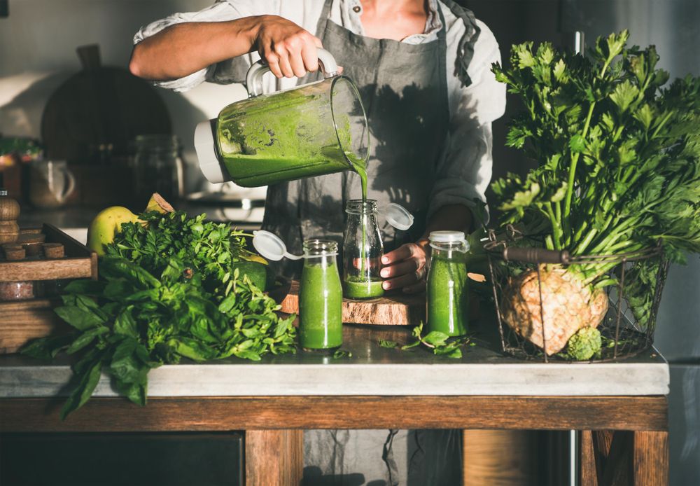 Woman pouring green smoothie into jars in kitchen