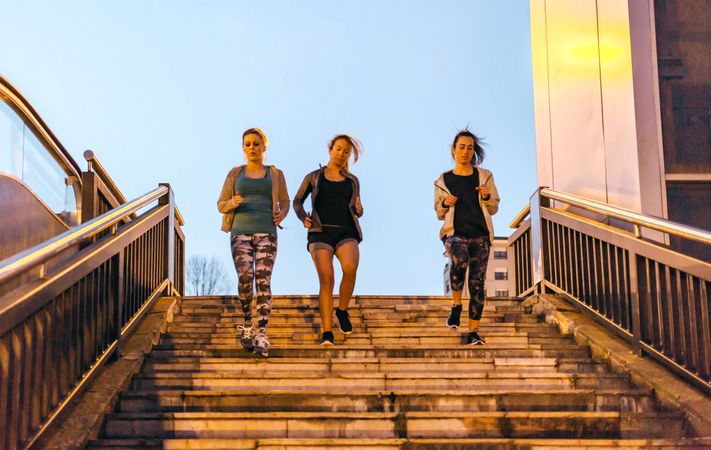 Women friends training running down stairs in town at sunset