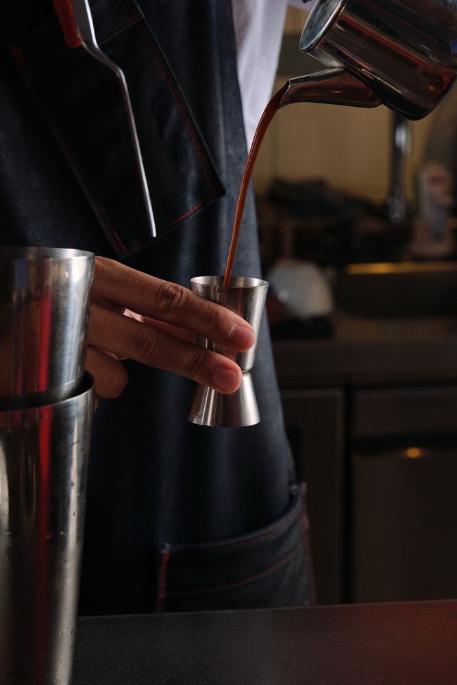 Crop bartender pouring coffee from kettle into jigger