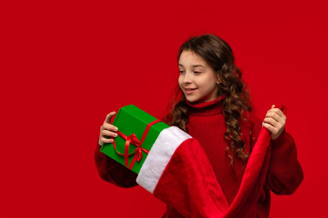 Smiling girl in red sweater holds gift and Santa hat.