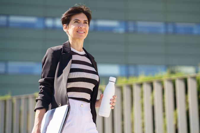 Smiling woman walking outside with computer and water bottle