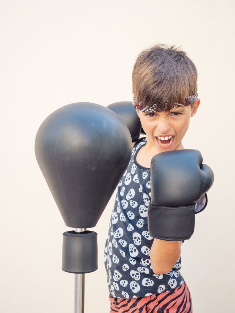 Sporty boy in boxing gloves beating punch bag