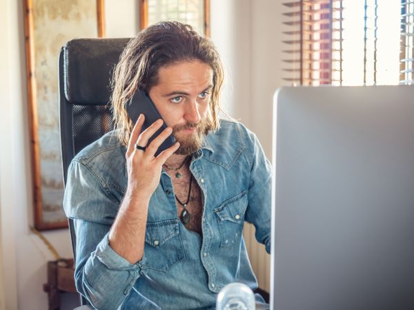 Attentive male browsing PC and talking on mobile in flat