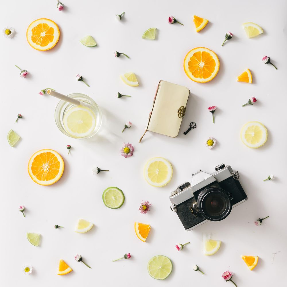 Colorful pattern made of orange, lemon, lime and flowers with lemonade and camera and notebook