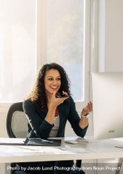 Woman sitting in front of computer in office discussing business on cell phone 0Pr9r4