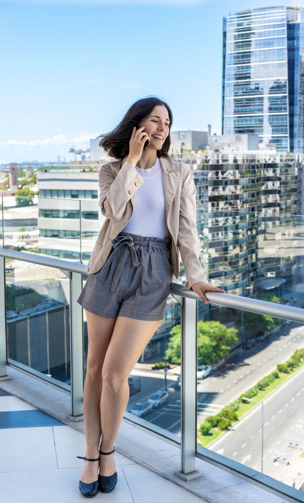 A woman is taking a break from work and chatting on her cell phone while standing on a balcony