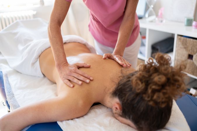 Masseuse kneading back of client in therapy room