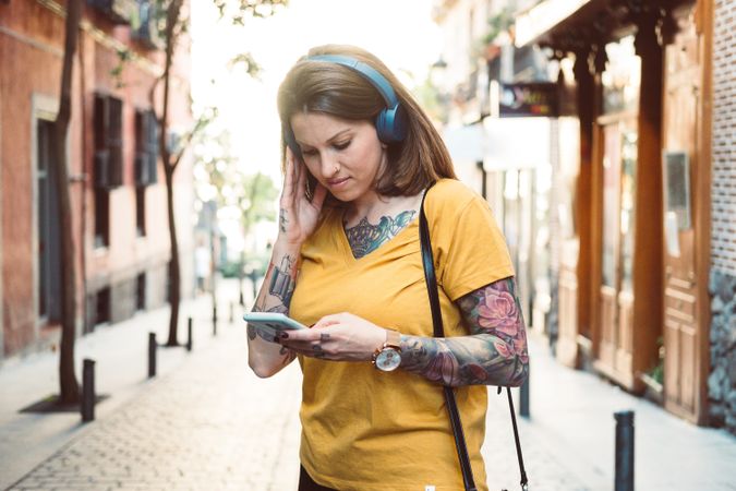 Inspired woman in headphones listening to music on smartphone on street