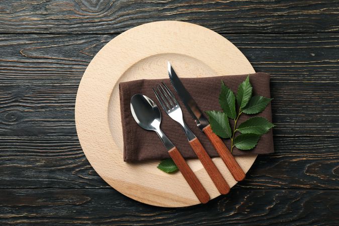 Table setting with wooden plate and cutlery on wooden background