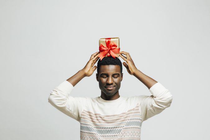Black man with his eyes closed holding present wrapped in gold and red above his head