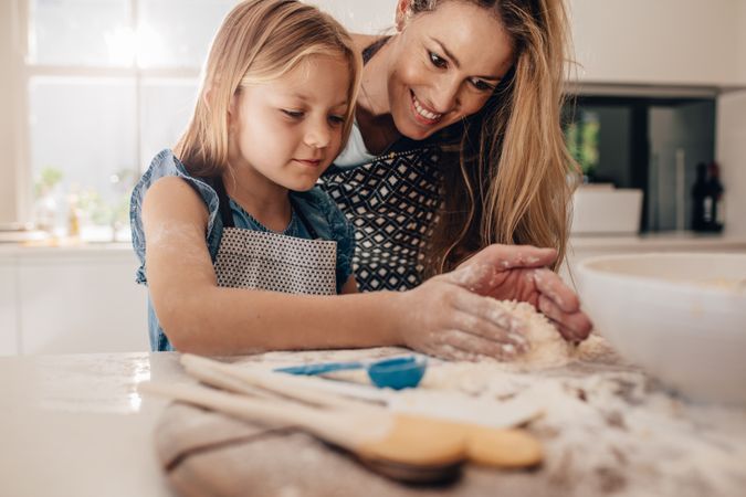 Little girl preparing dough on kitchen counter with her mother