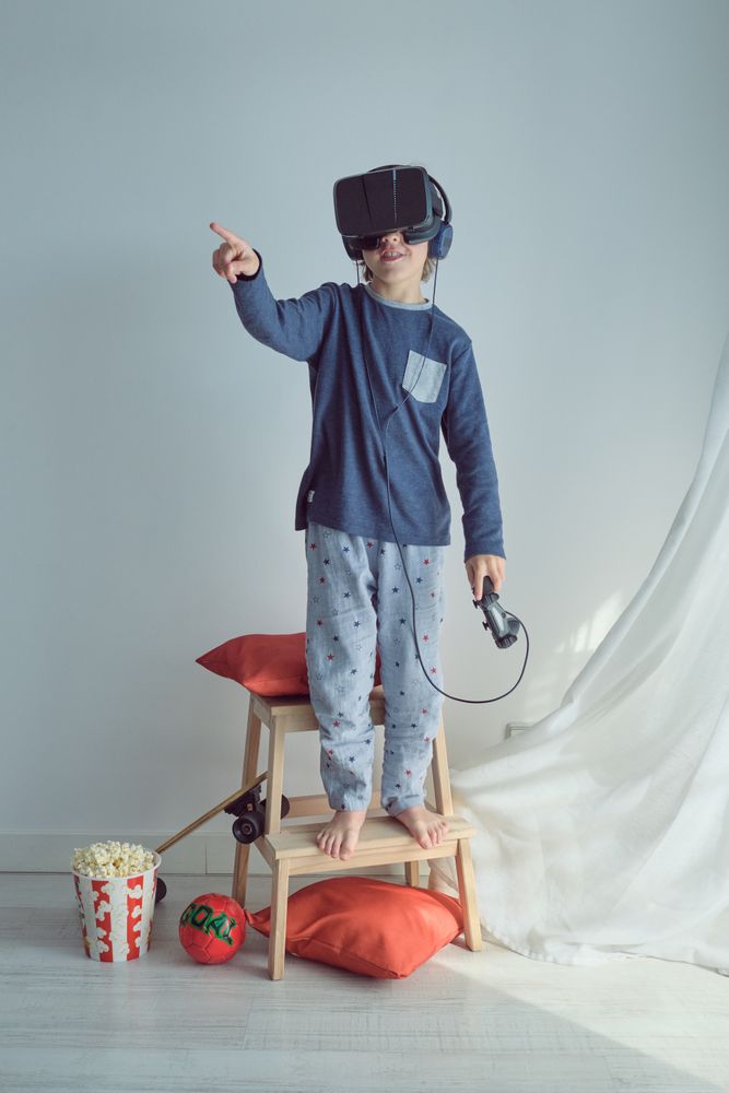 Adorable preteen boy in VR goggles and headphones with joystick