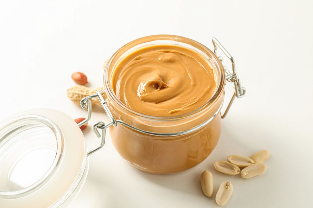 Composition with glass jar with peanut butter and peanut on light background, space for text and closeup