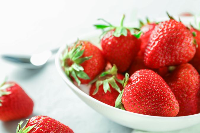 Plate with fresh strawberries and spoon on bright wooden background, closeup and space for text