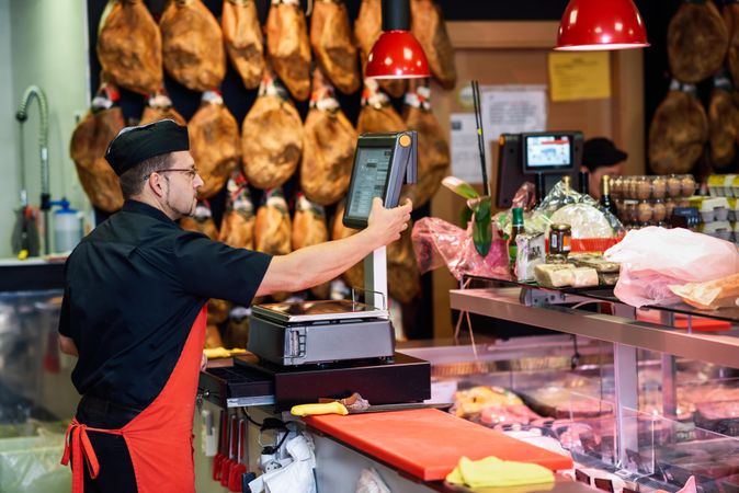 Man in butcher shop serving a customer at register behind the counter