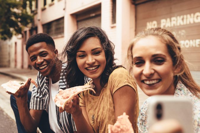 Woman taking selfie with friends while eating pizza