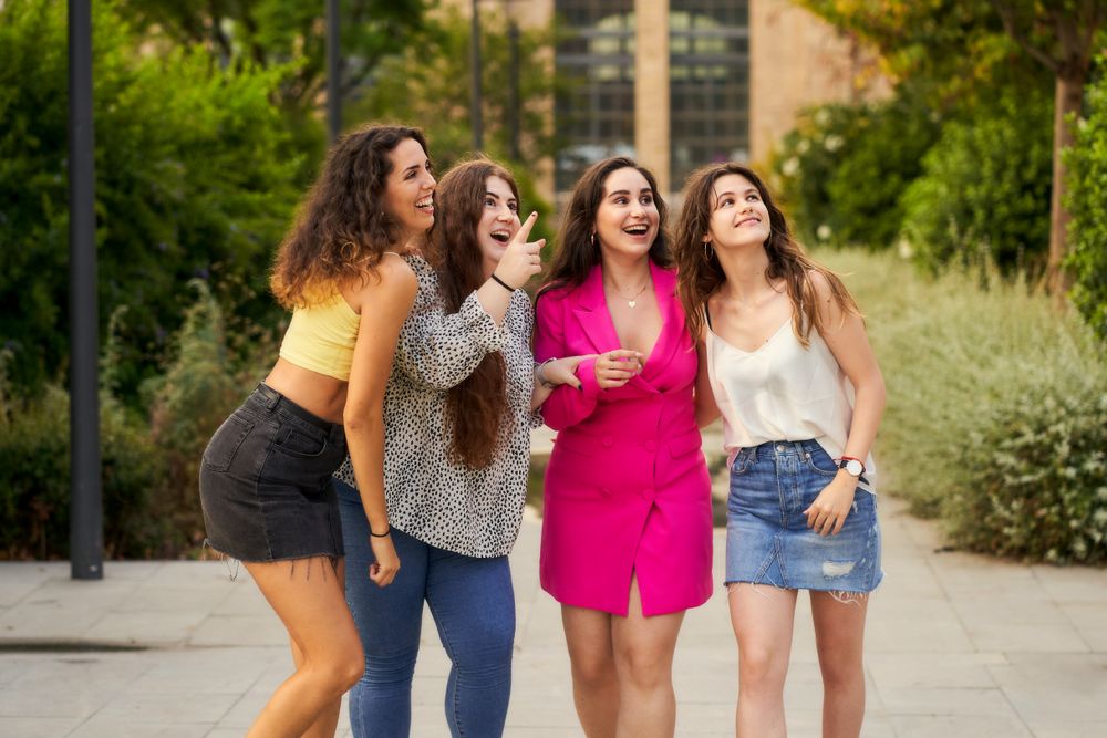 four smiling friends pointing upward and looking in that directi