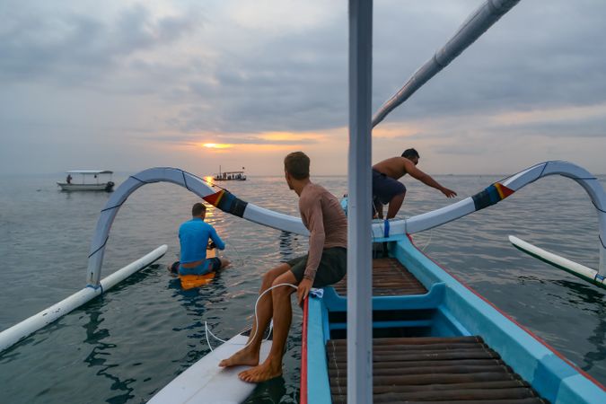 Men diving from boat in waving water at sunset