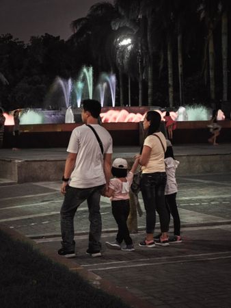 Back view of a family walking near water fountain at night