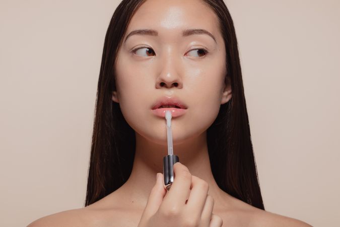 Portrait of beautiful young woman applying transparent lip gloss with applicator