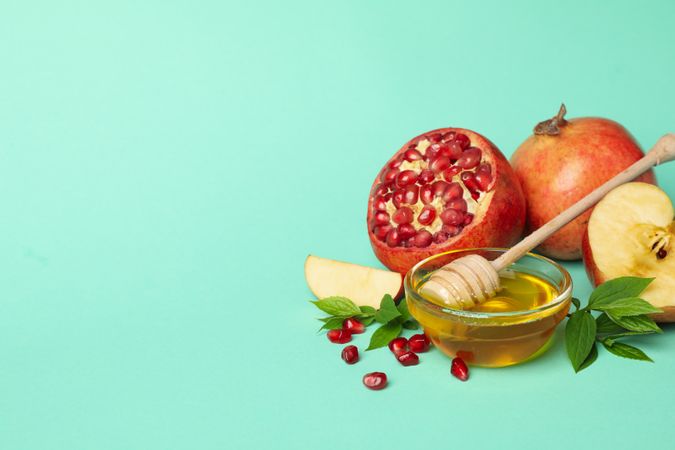 Open pomegranate, apple half, and honey in mint room with copy space