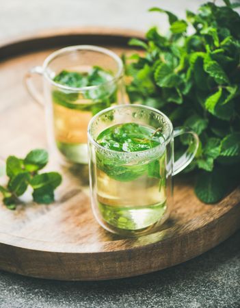 Mint tea with fresh mint leaves on wooden tray, close up
