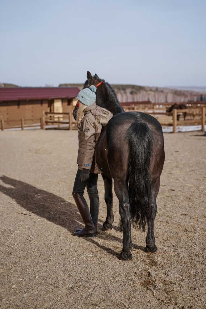 Warm dressed woman with brown horse by hay
