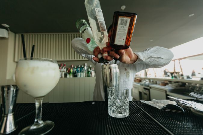 Barman pouring cocktail and alcoholic drinks to shaker in a bar.