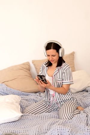 Woman reacting to smartphone content with headphones in bed.