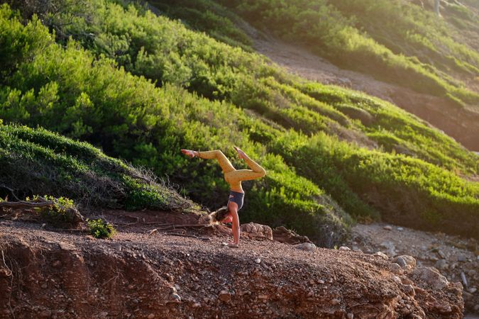 Woman taking Handstand pose with legs spread in nature