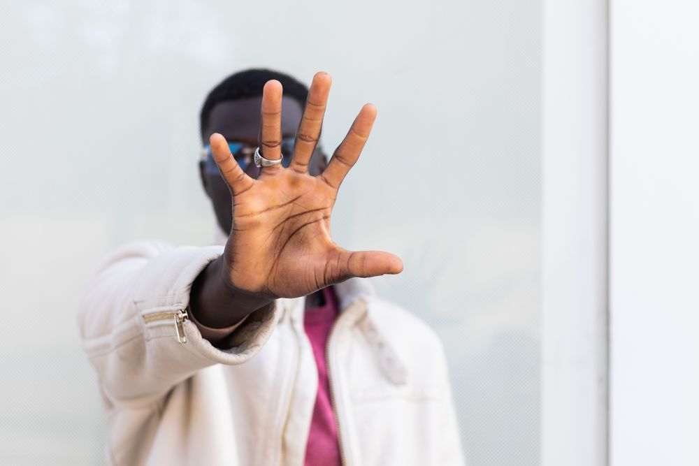 Black man covering face and showing stop gesture in city street