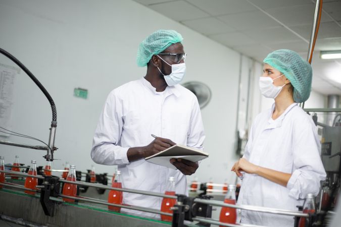 Two diverse factory workers are inspecting machinery inside a beverage production facility.