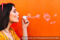 Young woman having fun blowing bubbles against orange wall 5aJWG4
