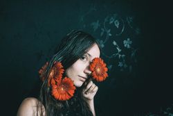 Studio portrait of mature woman with blue eyes holding gerbera flowers