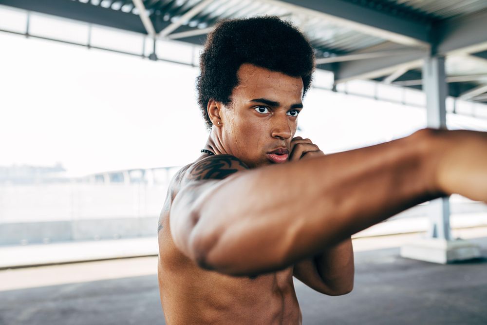 Athletic Black male throwing a punch during training under a bridge