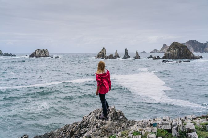 Woman on stony seashore looking on foamy water washing peaks